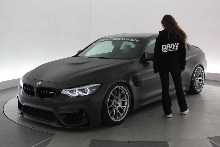 Drive Sideways Hoodie päällä BMW M4:n vieressä