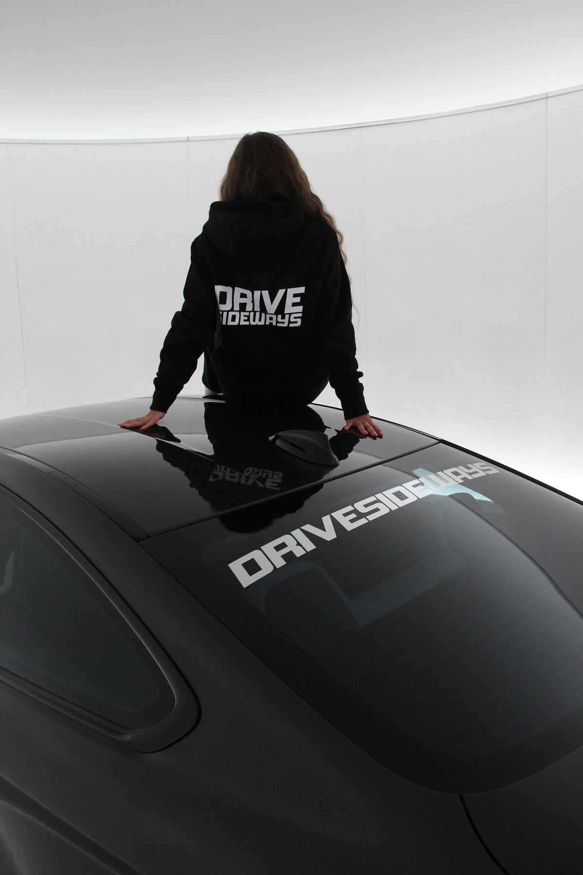 Drive Sideways Hoodie päällä, malli istuu auton katolla