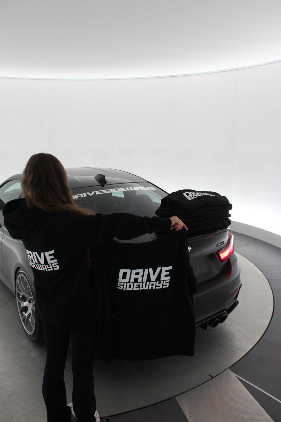 Drive Sideways Hoodie kädessä auton takana